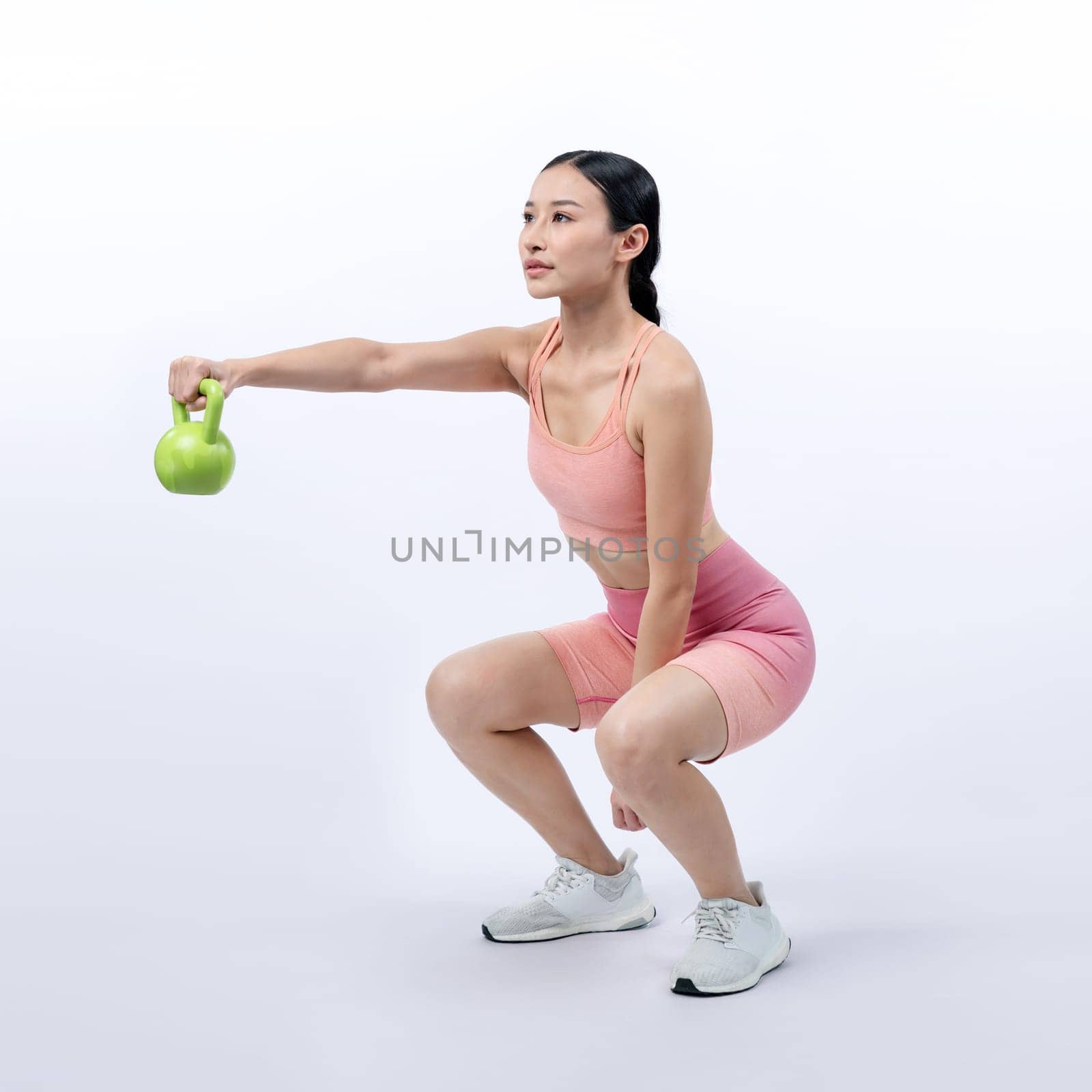 Vigorous energetic woman doing kettlebell weight lifting exercise on isolated background. Young athletic asian woman strength and endurance training session as body workout routine.