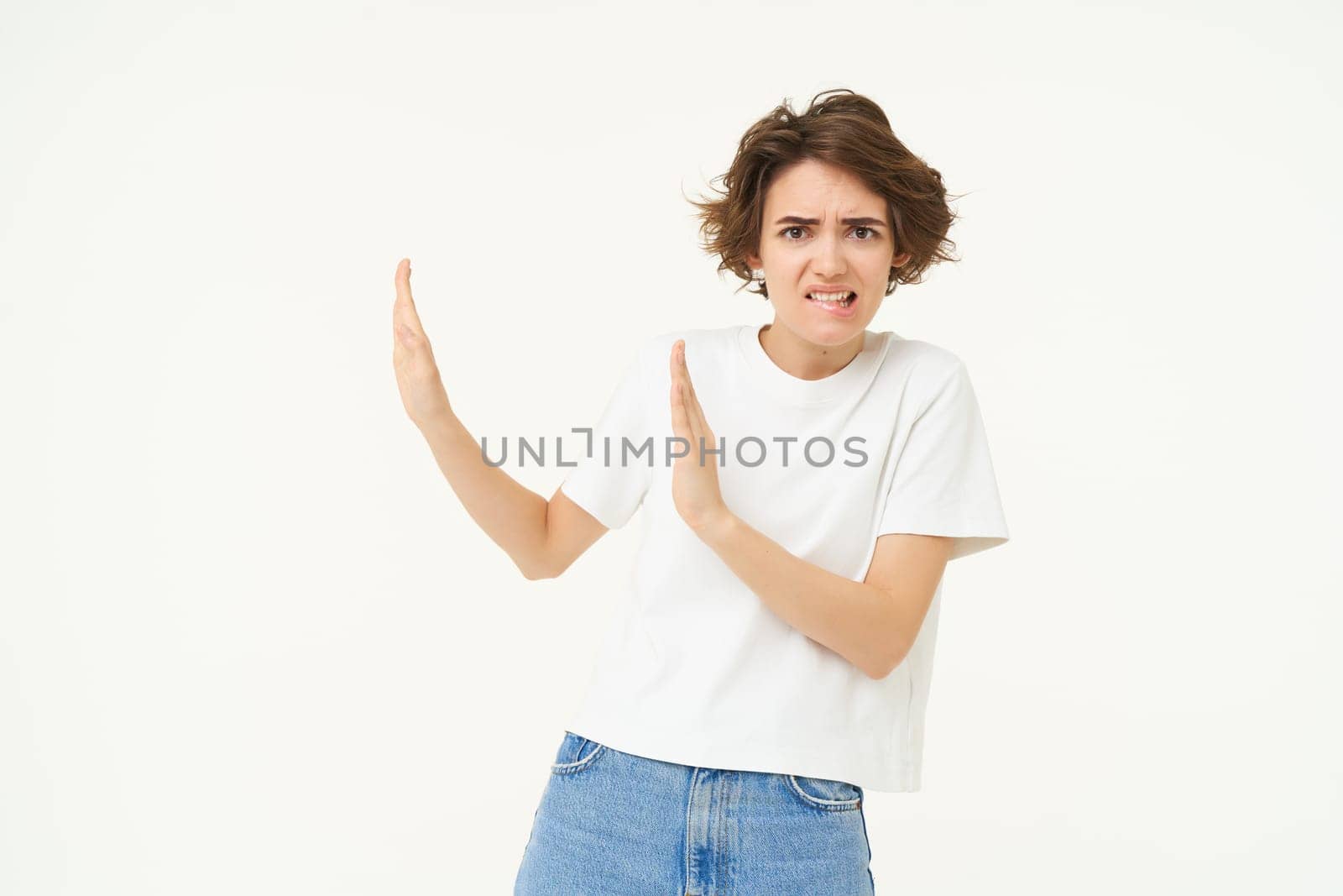 Portrait of woman avoiding someone, shows block hands gesture and refusing from something bad, standing over white background.