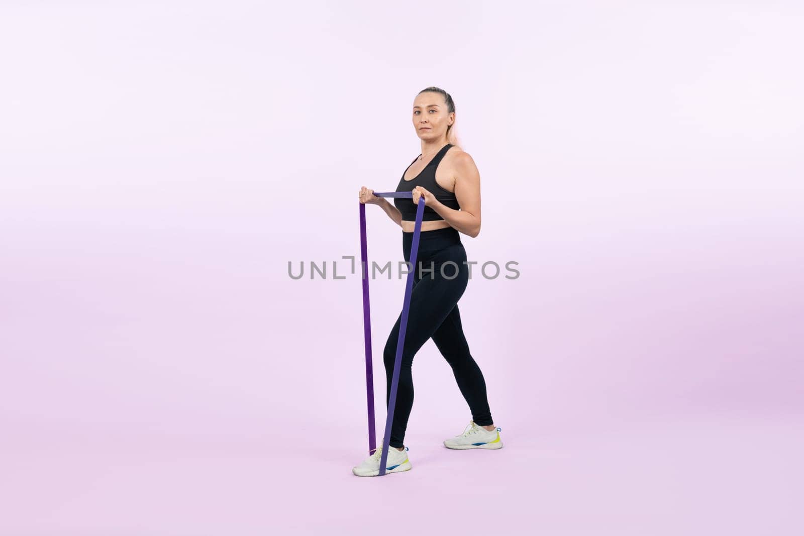 Full body length shot athletic and sporty senior woman with fitness resistance band on isolated background. Healthy active physique and body care lifestyle after retirement. Clout