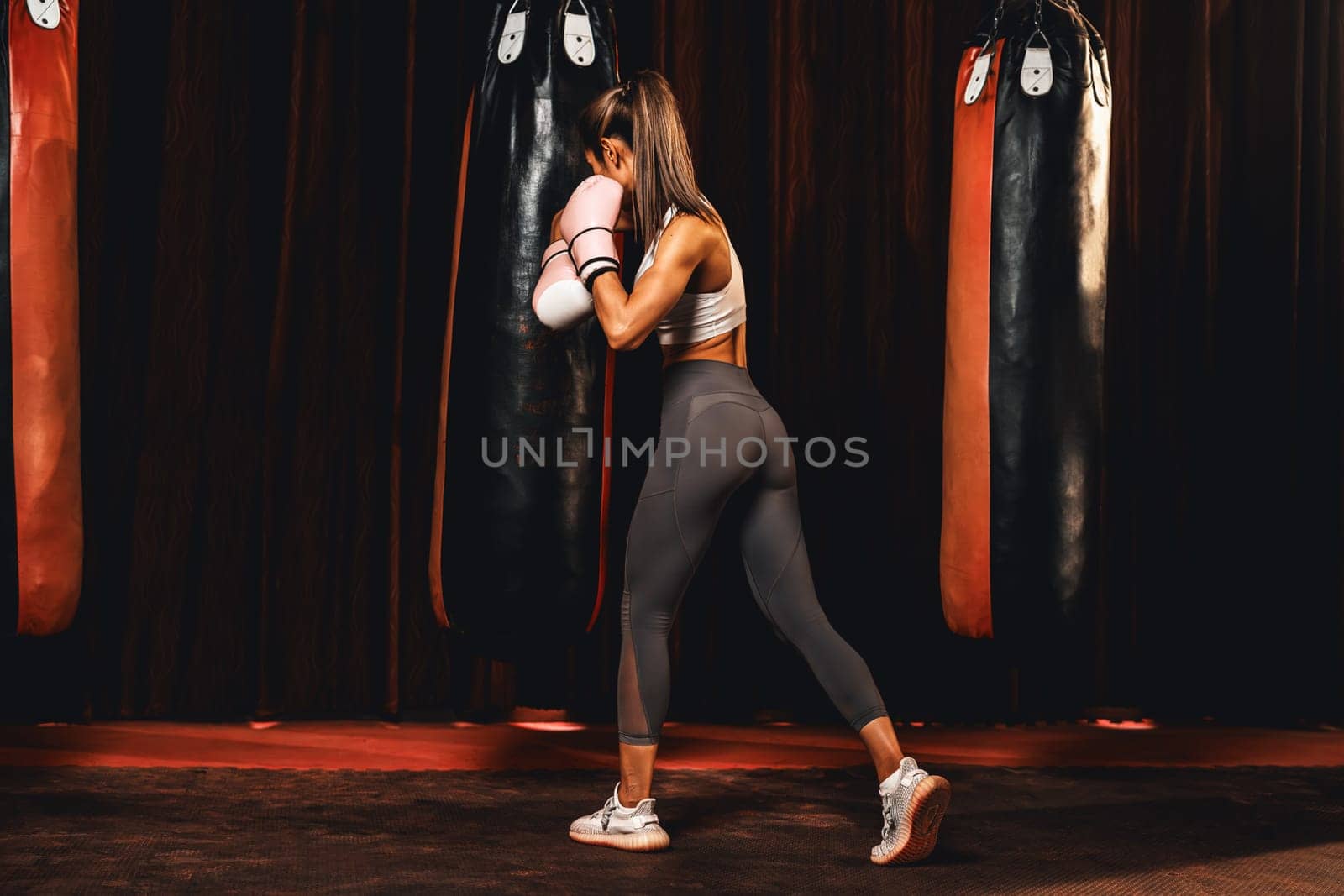 Asian female Muay Thai boxer in sport wear punching at bag. Impetus by biancoblue
