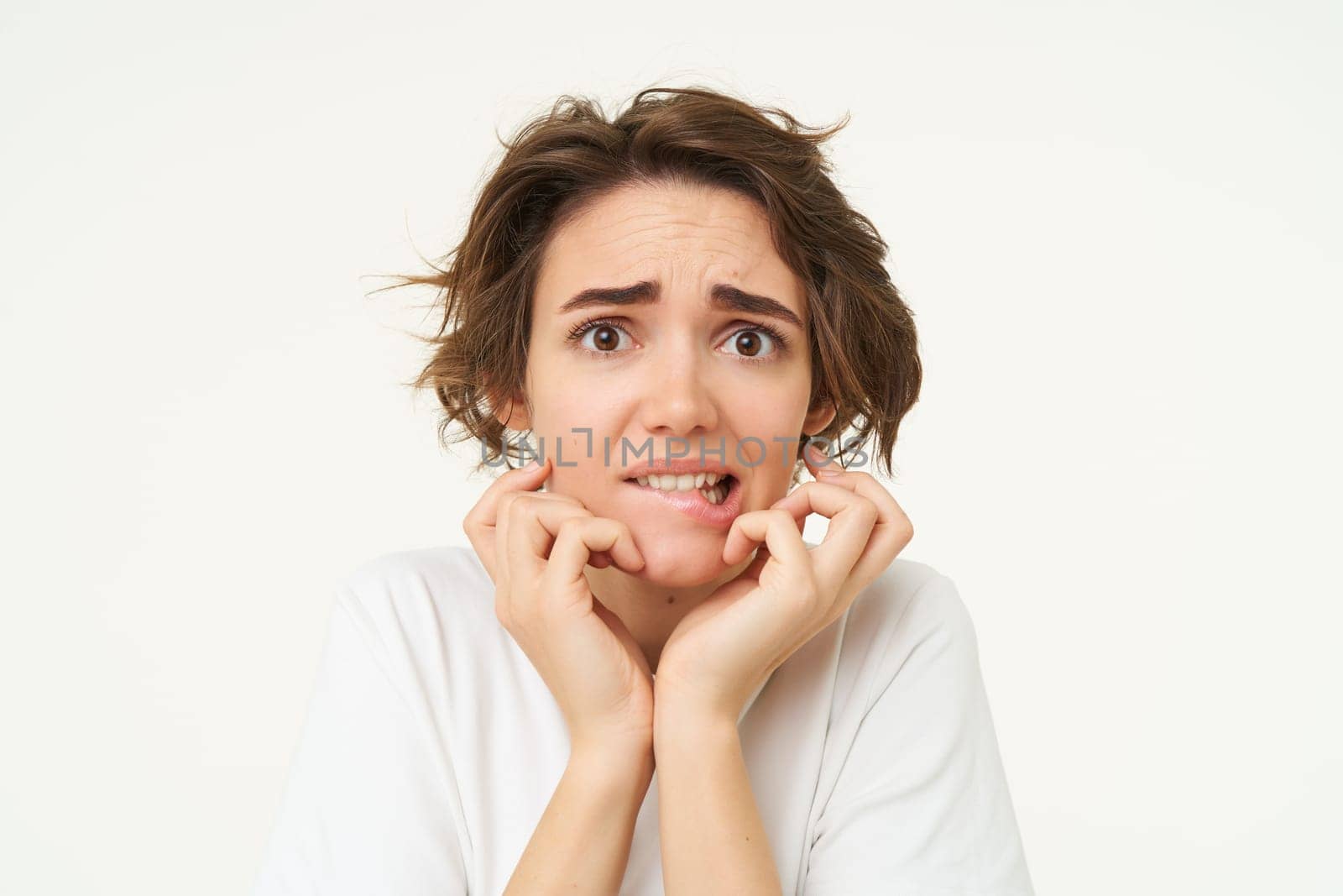 Close up of scared brunette woman, shaking from fear, looking concerned and frightened, standing over white studio background by Benzoix