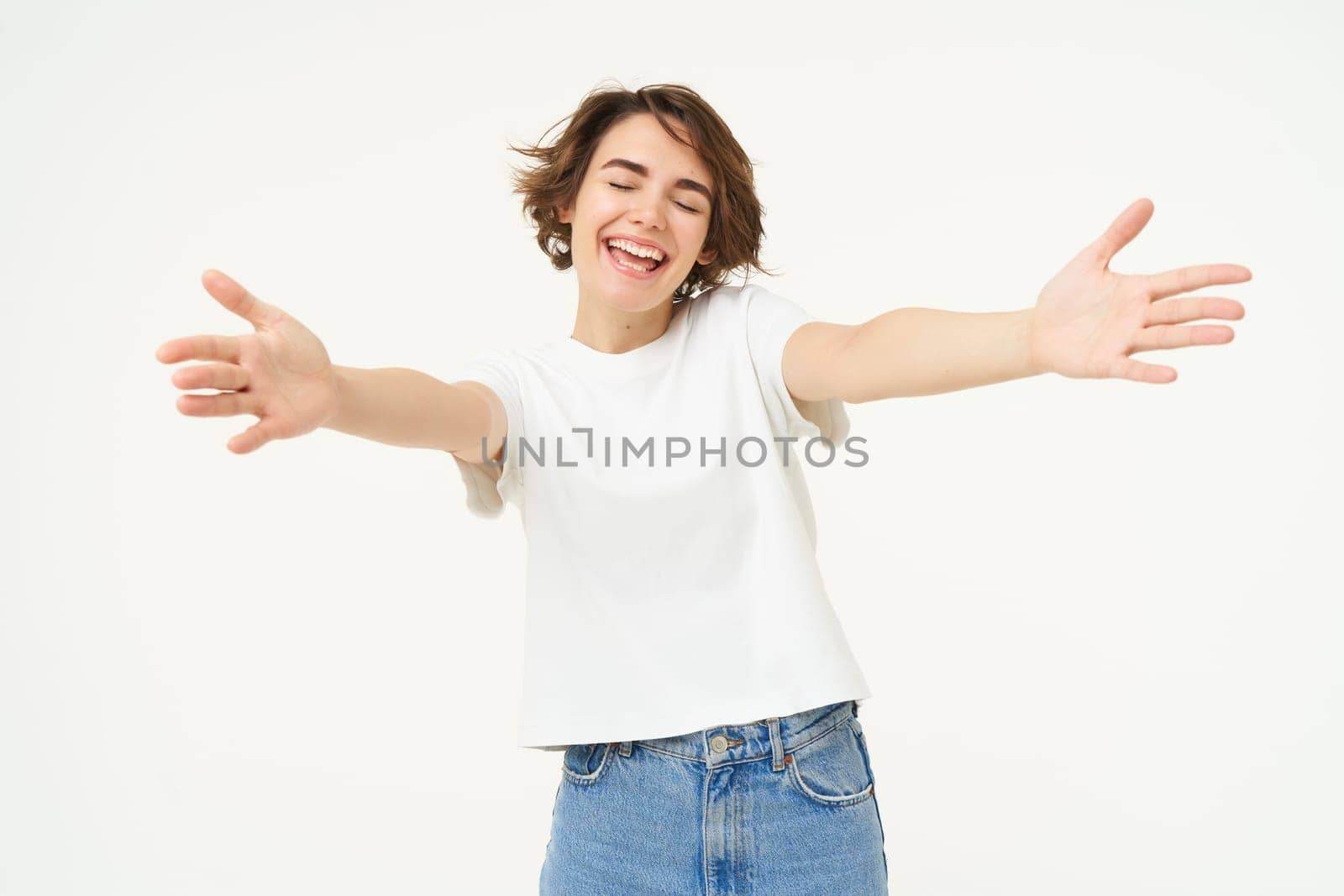 Portrait of happy woman inviting for hug, extends hands forward and hugs, cuddle friend, stands over white studio background.
