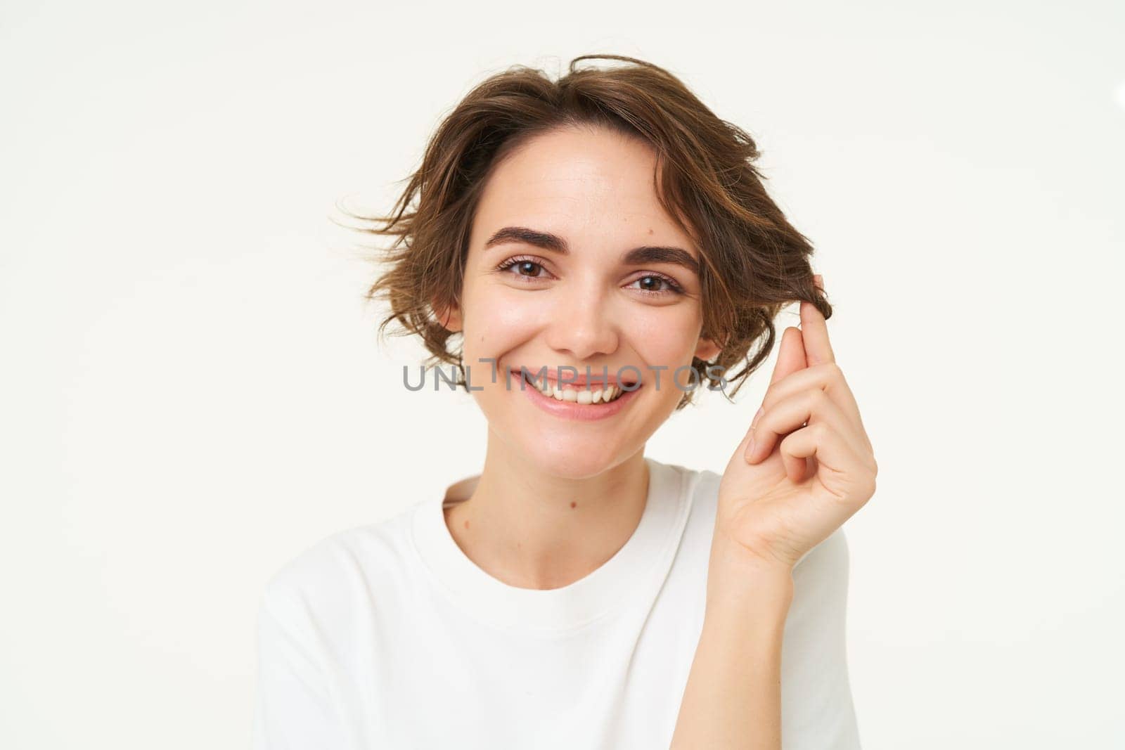 Close up portrait of brunette woman smiling, playing with hair strand, showing new haircut, posing over white studio background by Benzoix