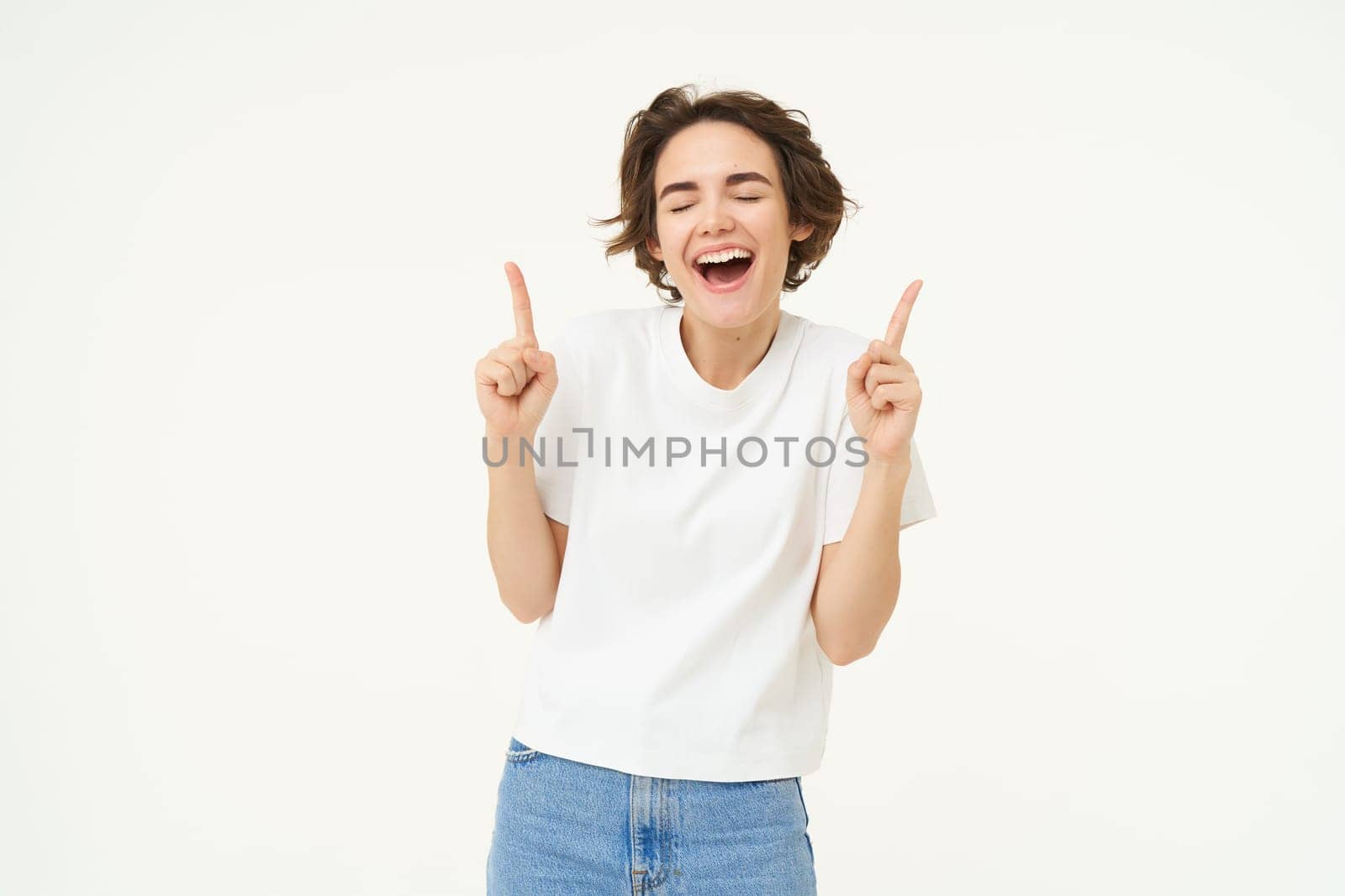 Image of carefree girl, laughing and smiling, pointing fingers up, showing promo offer, banner on top, posing over white studio background. Copy space