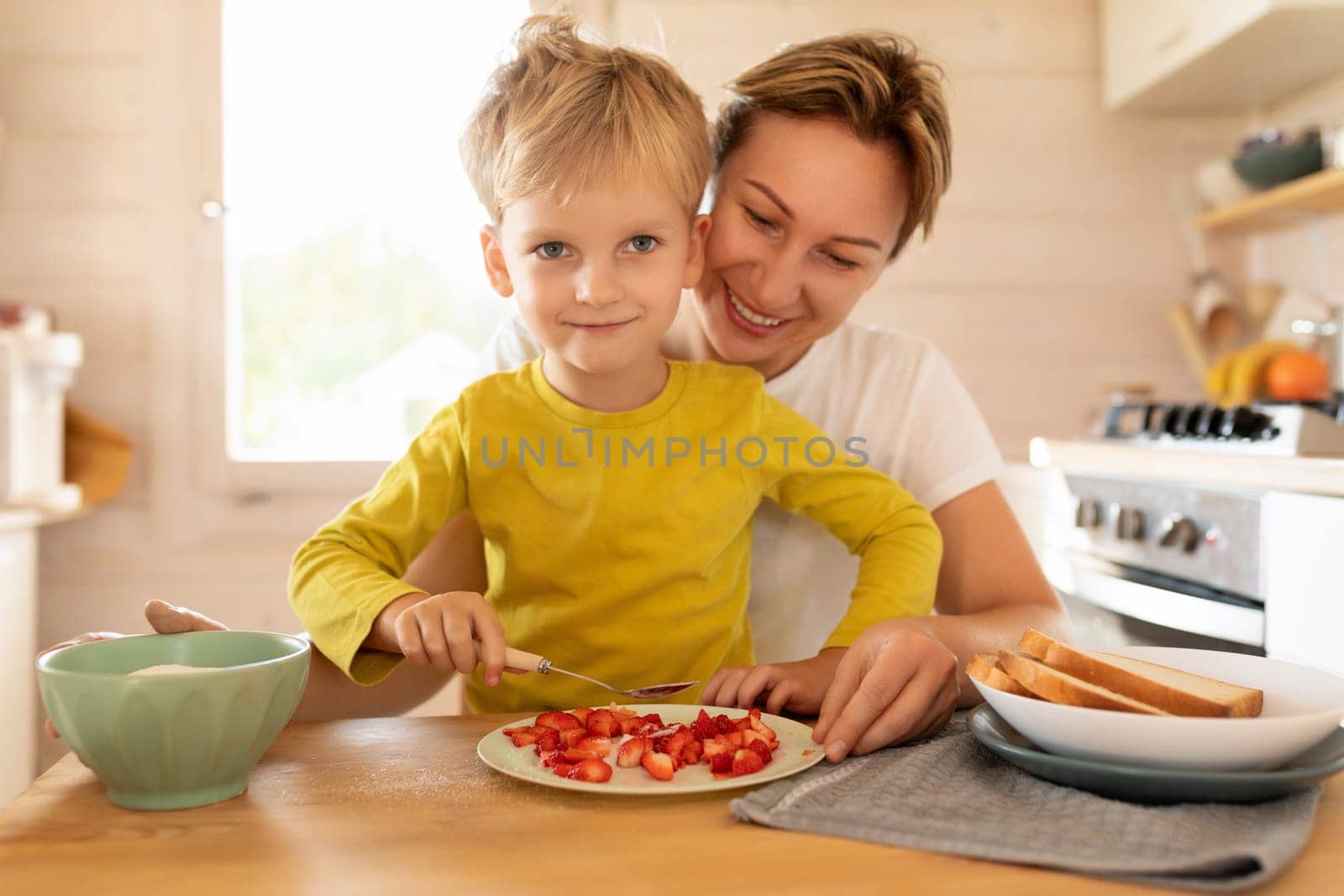 lifestyle concept, young mother and son sitting at the table in the kitchen with plates of food by TRMK