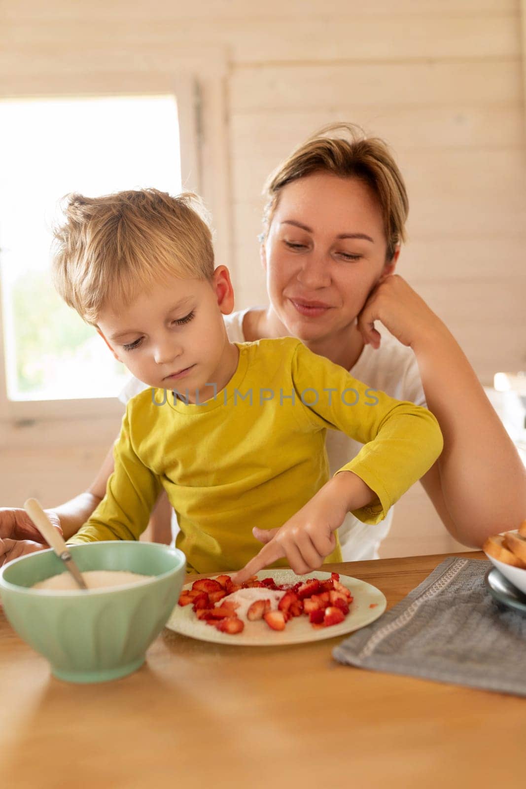 cheerful Caucasian mother and little son are sitting in the kitchen and preparing breakfast.