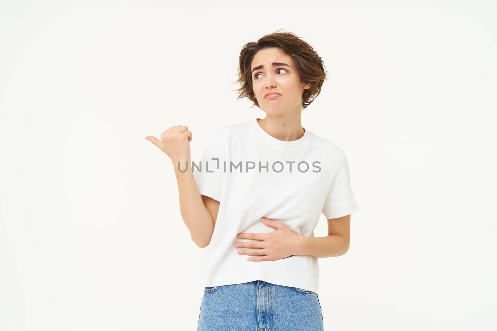 Image of sad woman with stomach ache, points left, shows banner with advertisement, touches her belly, has painful menstrual cramps, isolated over white background.