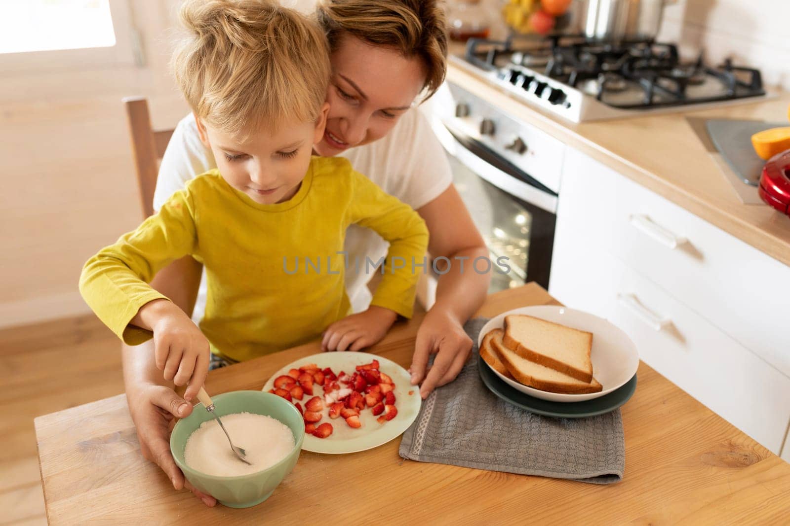 happy mother and little son preparing toast with strawberries for breakfast by TRMK