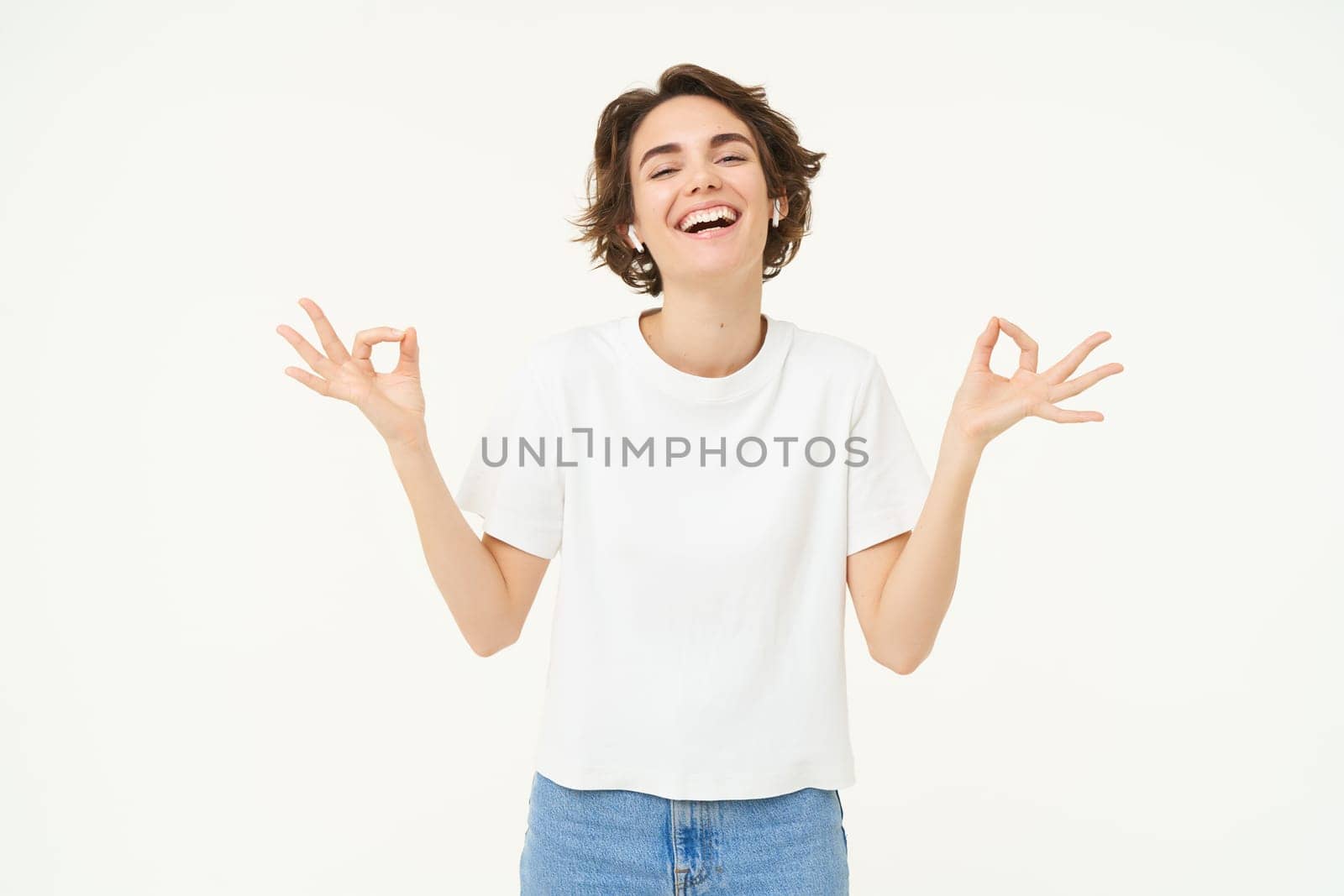 Portrait of young woman feeling peace and relaxation, holding hands sideways, zen gesture, meditating, practice mindfulness yoga, standing over white background.