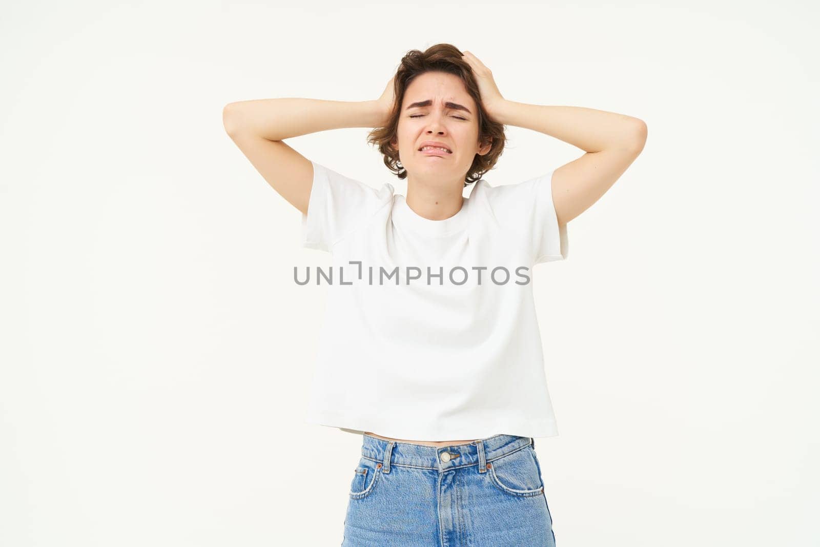 Portrait of troubled woman, holds hands on head and panicking, feeling upset, depressed, stands over white studio background.