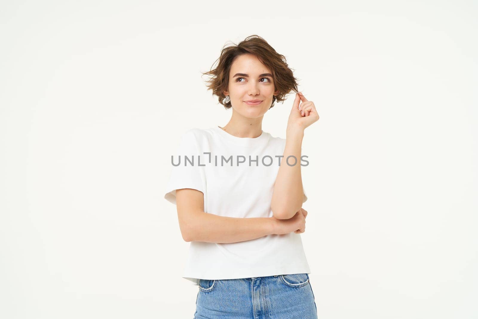 Portrait of thoughtful brunette girl, playing with her curl and thinking with smiling face, standing over white background.