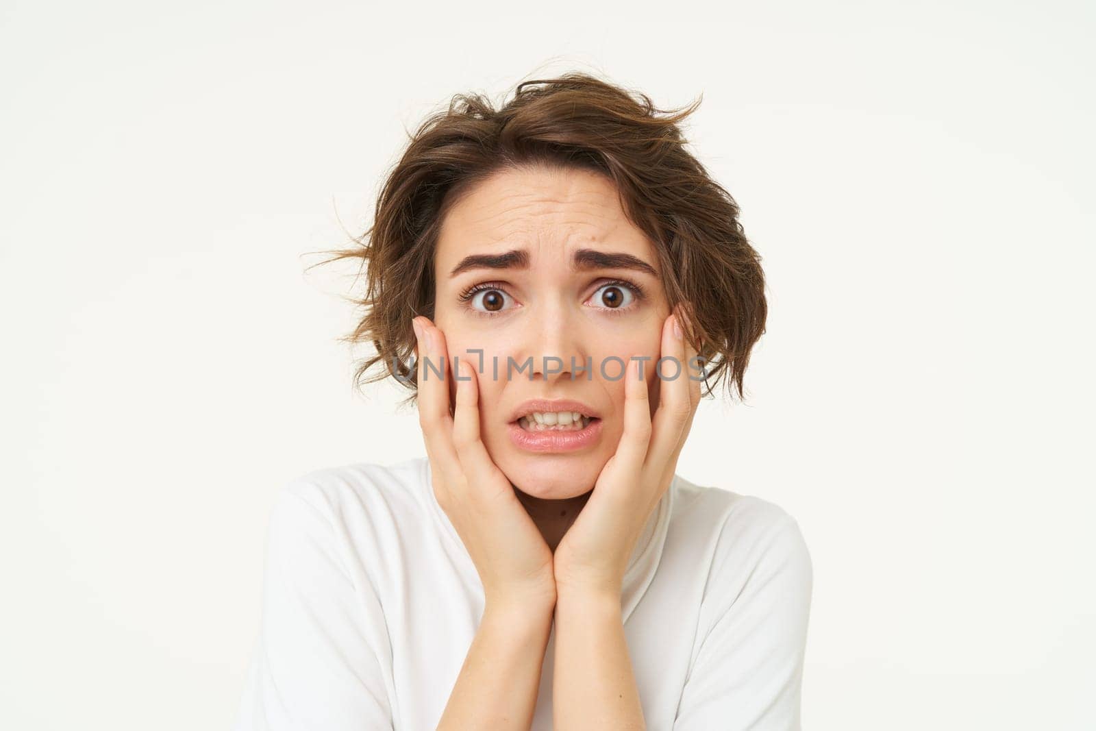 Close up shot of scared woman in panic, touches her face and shaking from fear, posing over white background. Copy space