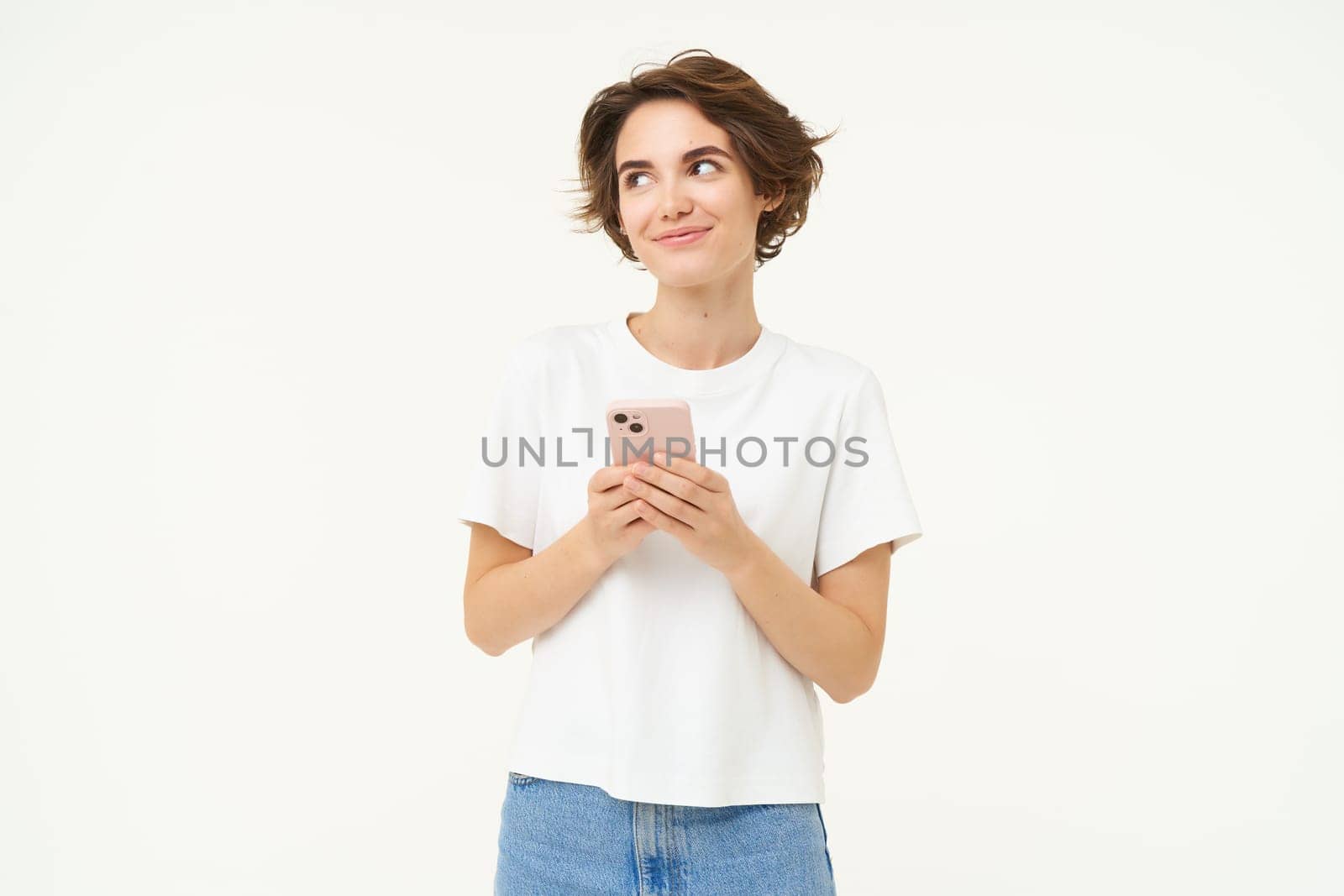 Portrait of brunette woman using smartphone, standing with mobile phone, texting, placing an order, browsing social media in telephone, standing over white background.