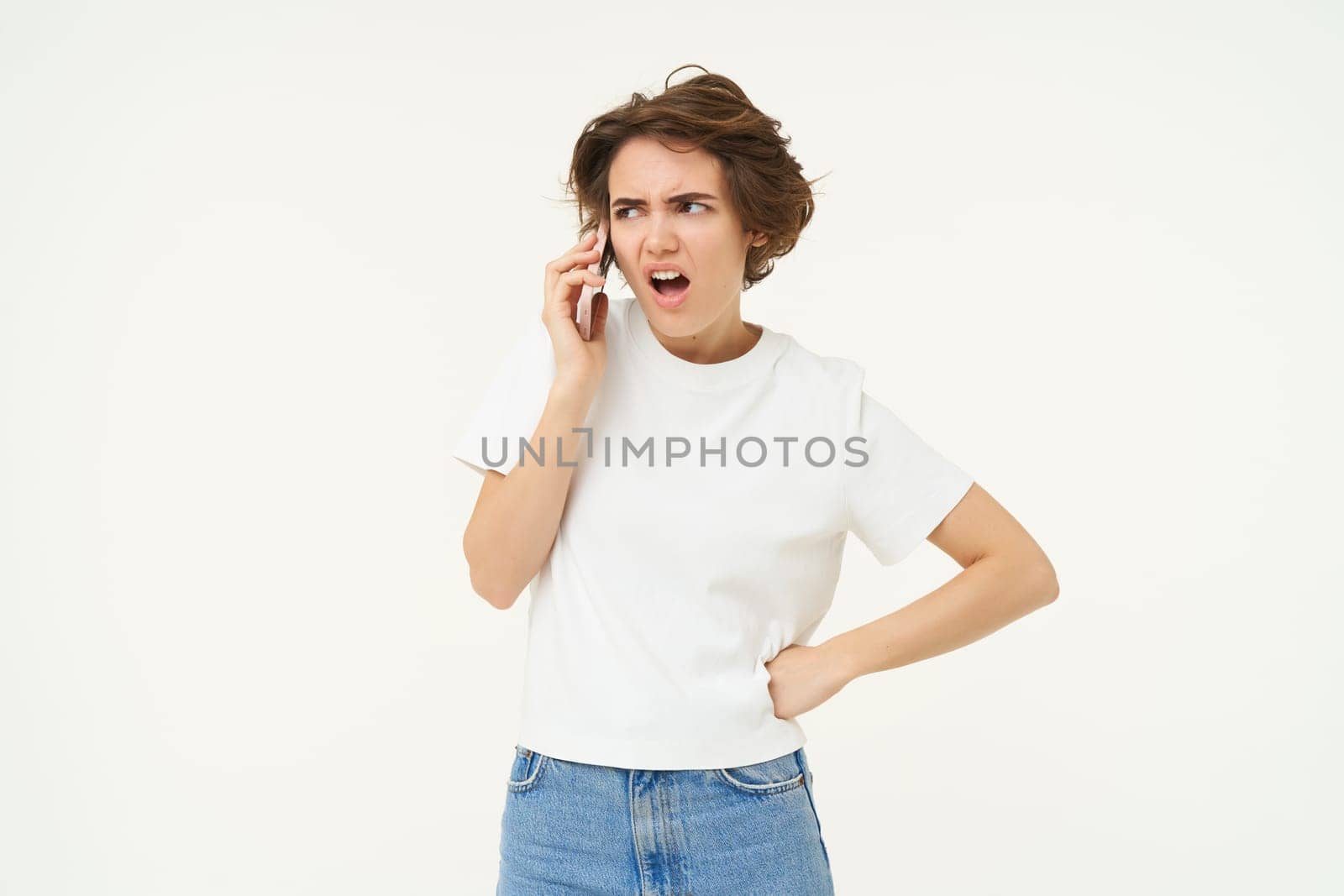 Annoyed girl arguing on mobile phone, talking, having an argument over the telephone, standing over white background.