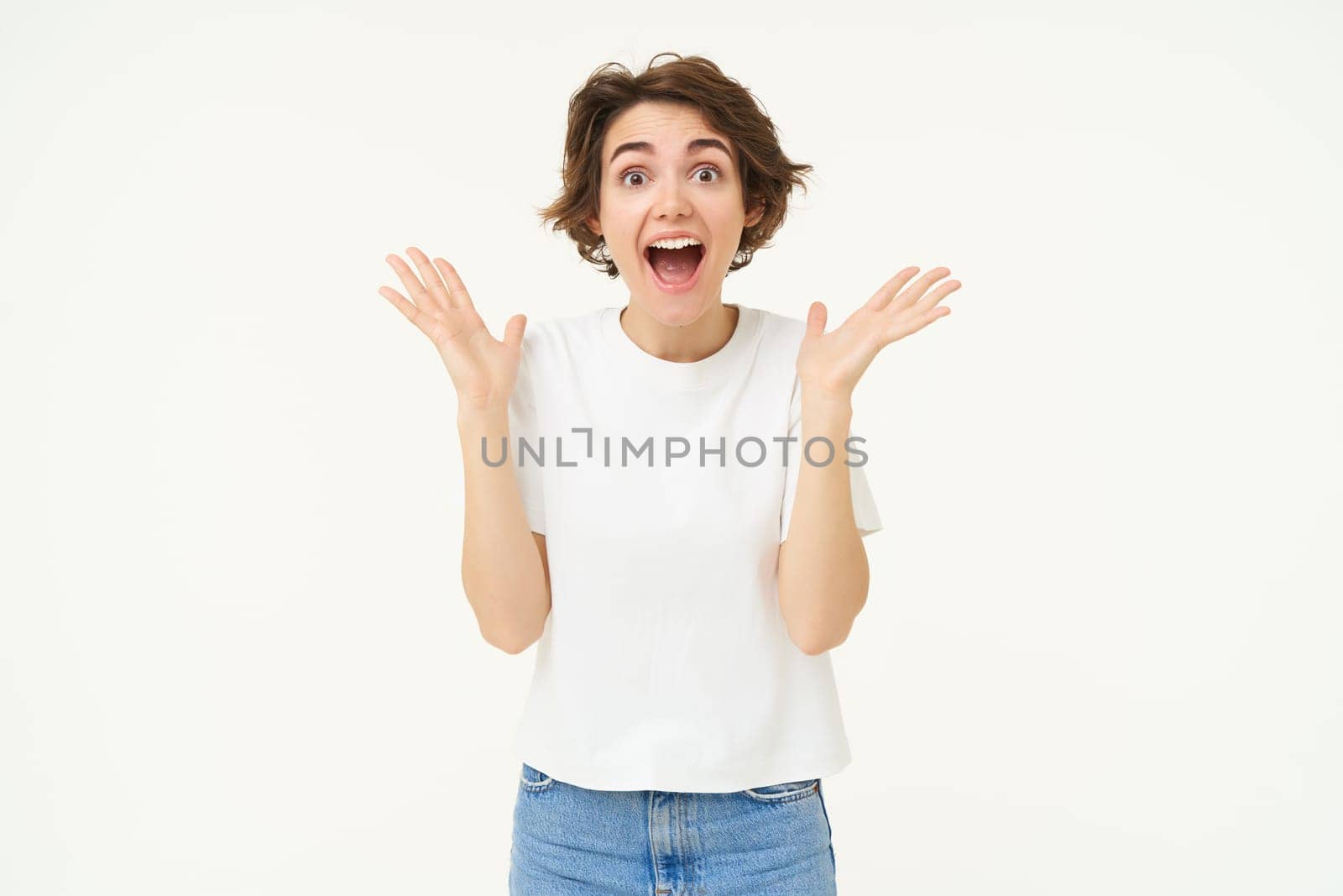 Portrait of surprised brunette woman looks surprised, gasping amazed, reacts to amazing big news, stands over white background.