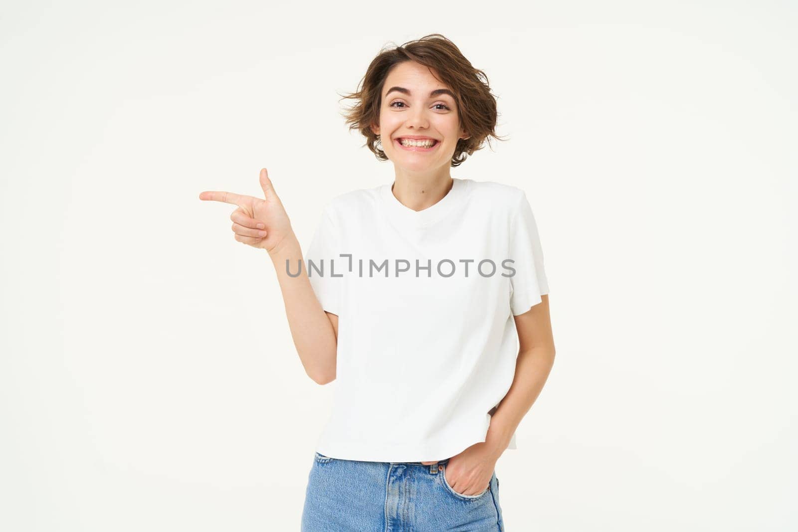 Image of cute woman with happy smile, pointing left, showing advertisement, standing over white background. Copy space