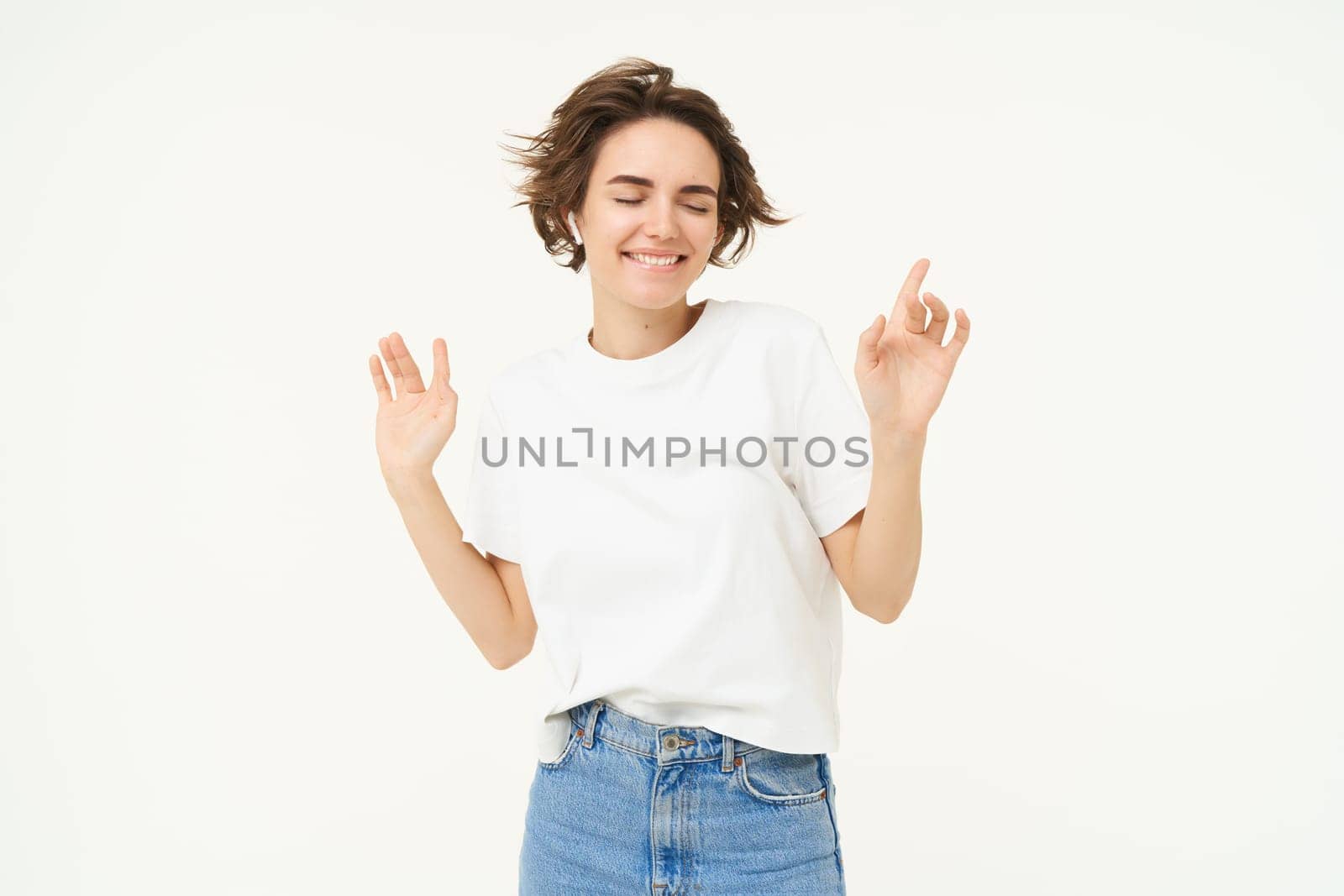 Portrait of happy young woman dancing, having fun, enjoying the music, posing over white studio background. Copy space