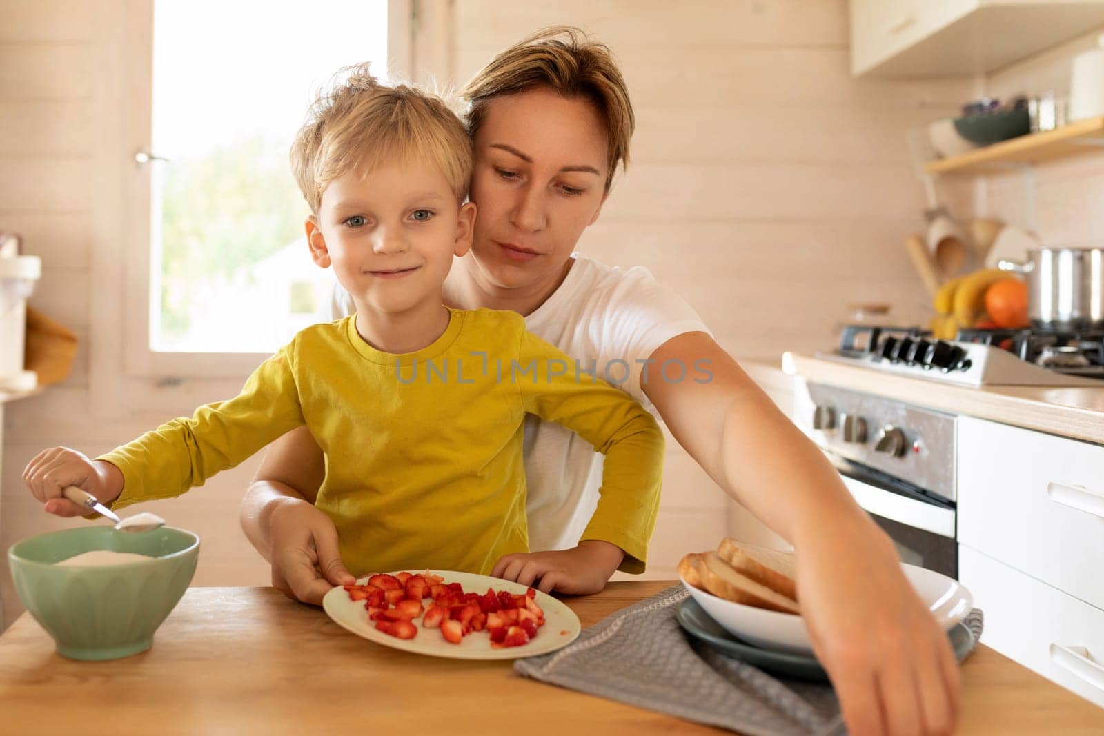young mother and son sitting at the table and preparing breakfast at home, happy motherhood by TRMK