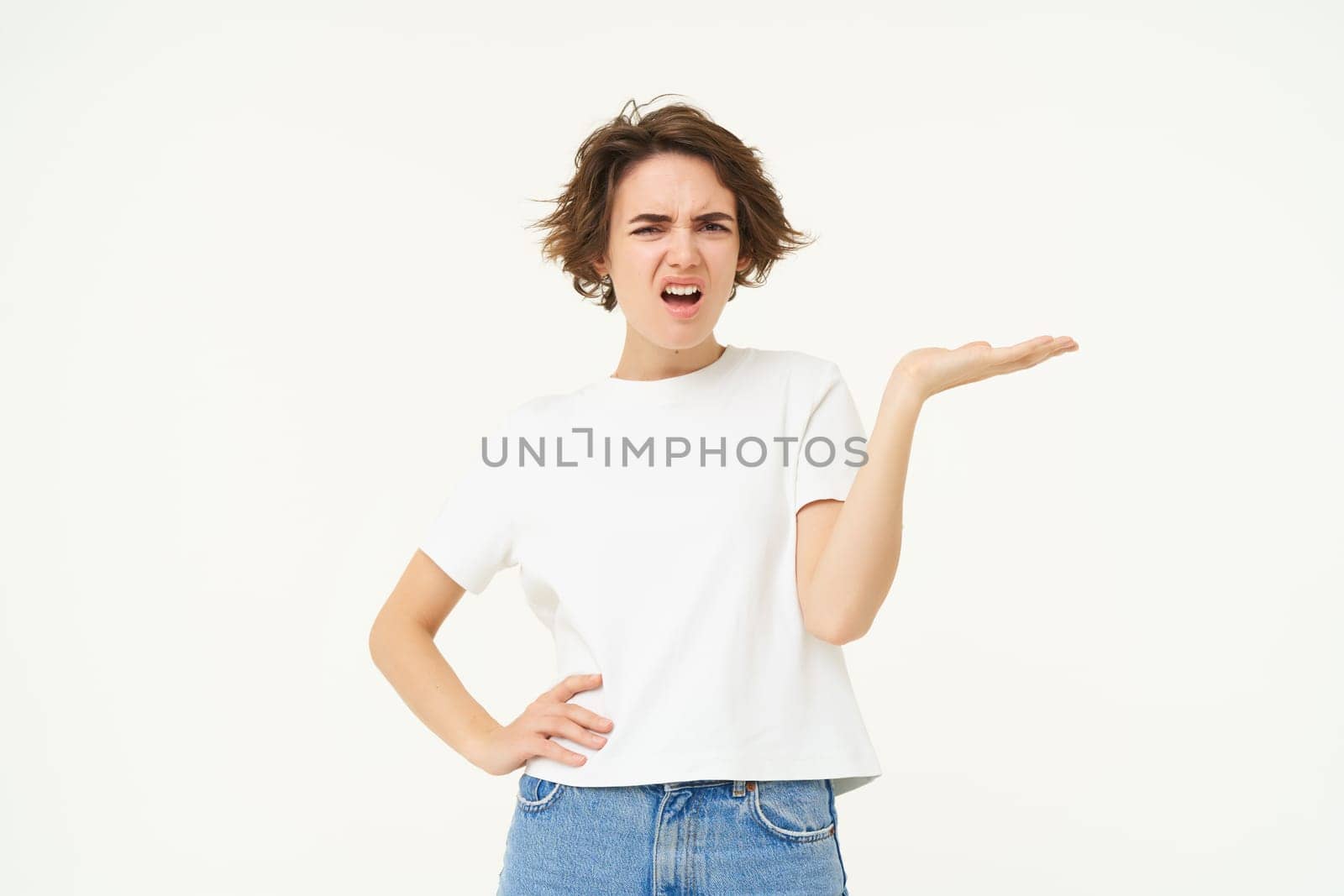 Portrait of woman complaining, raising hand up with frustration, looking angry, standing over white background. Copy space