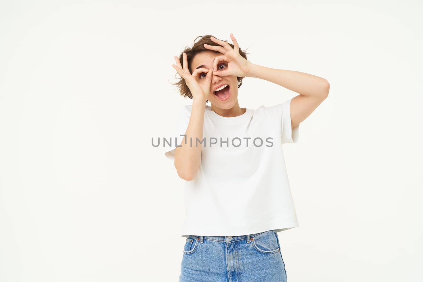 Portrait of happy woman making fun hand glasses over eyes and laughing, isolated over white background.