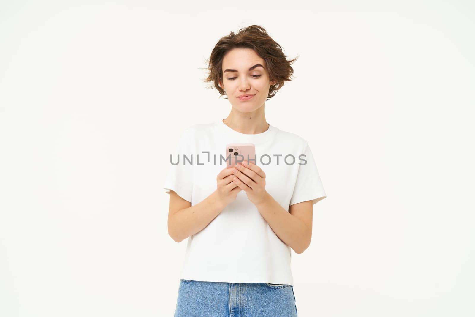 Portrait of brunette girl with smartphone, sending a message, using mobile phone application, smiling and looking happy, white studio background.