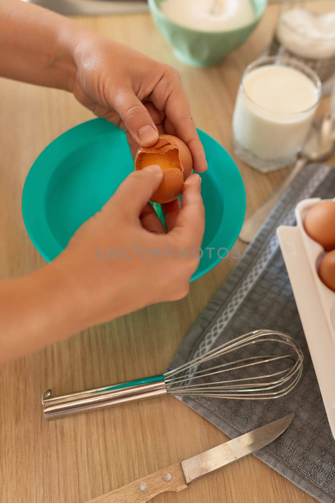 A woman breaks eggs into a deep bowl.