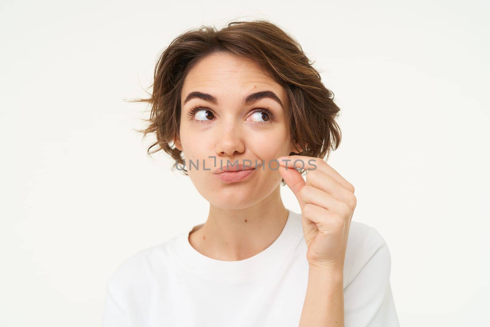 Image of young woman makes promise to keep secret, shows mouth zip gesture, puts a seal on her lips, dont talk sign, stands over white background.