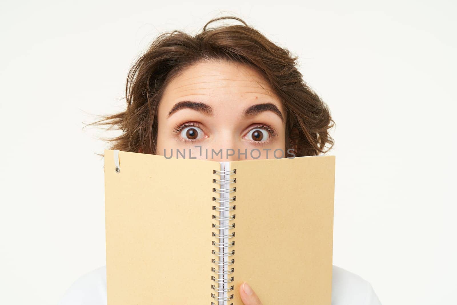 Close up portrait of girl face, hiding behind notebook, looking aside, standing over white background by Benzoix