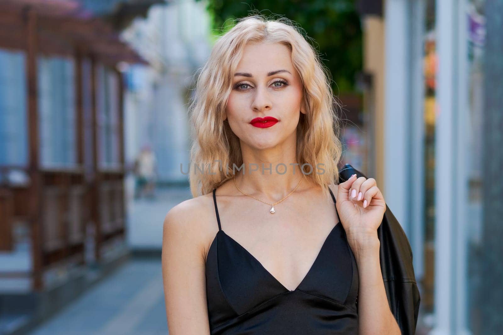 beautiful blonde woman with red lipstick in black top and leggings posing on street in the city