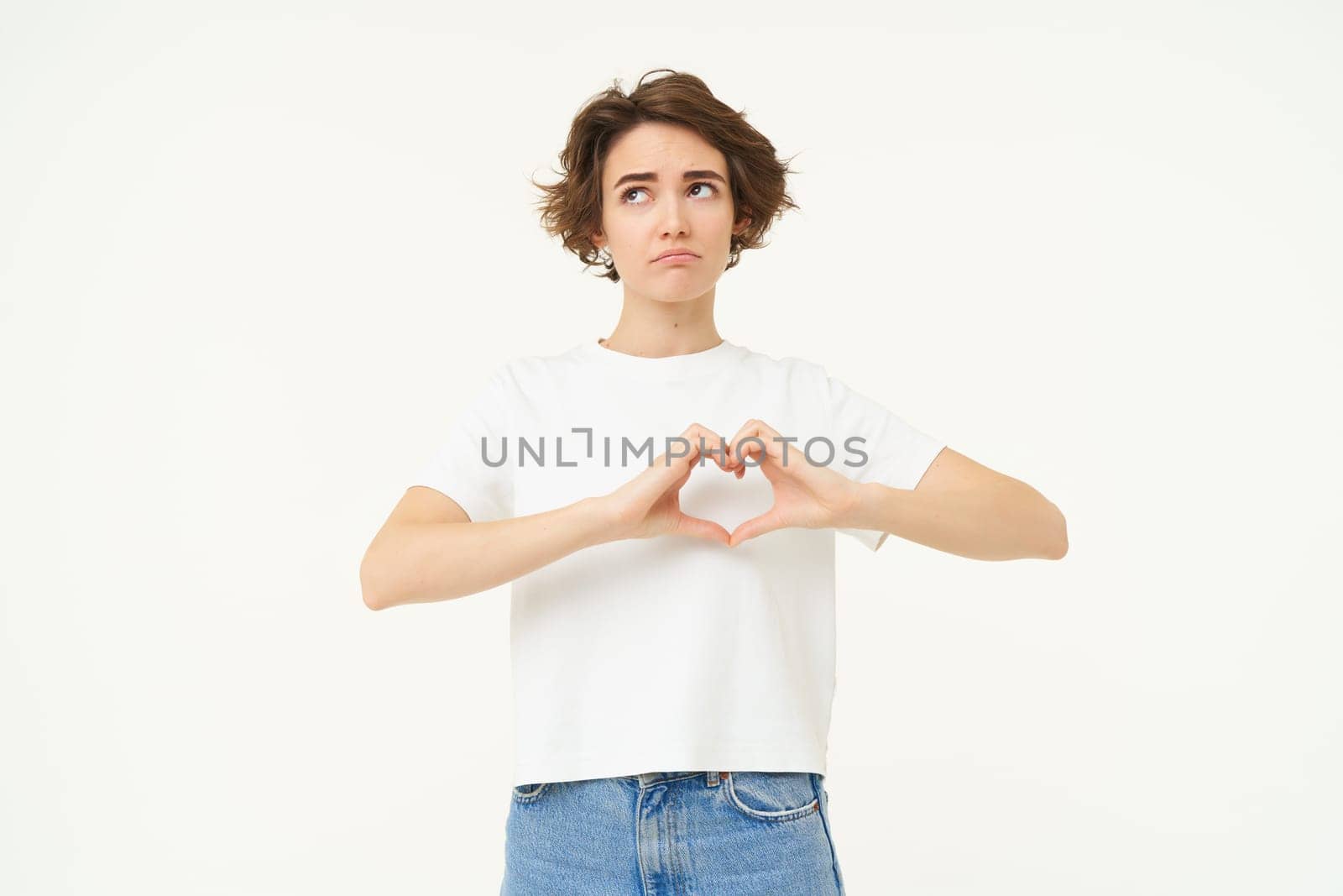 Portrait of brunette girl shows heart sign, love gesture, express care and warm feelings, stands over white background by Benzoix