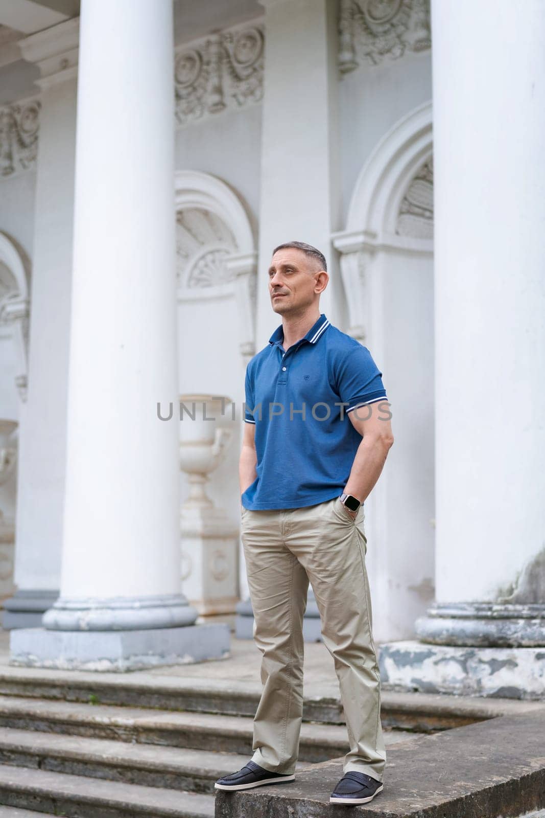 a man in casual clothes stands near the columns of a white building