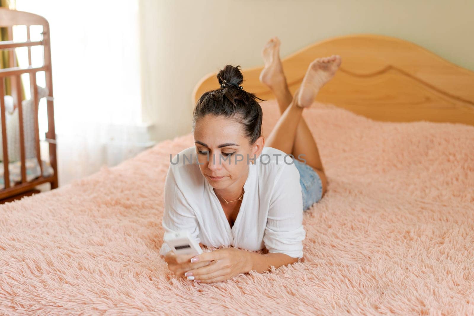 cute woman lying on the bed with a phone in her hand on a soft pink blanket by EkaterinaPereslavtseva