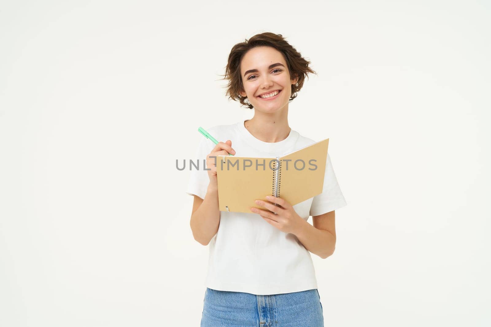 Portrait of smiling, beautiful and creative woman, holding pen and notebook, writing in her planner, has a diary, posing over white studio background.