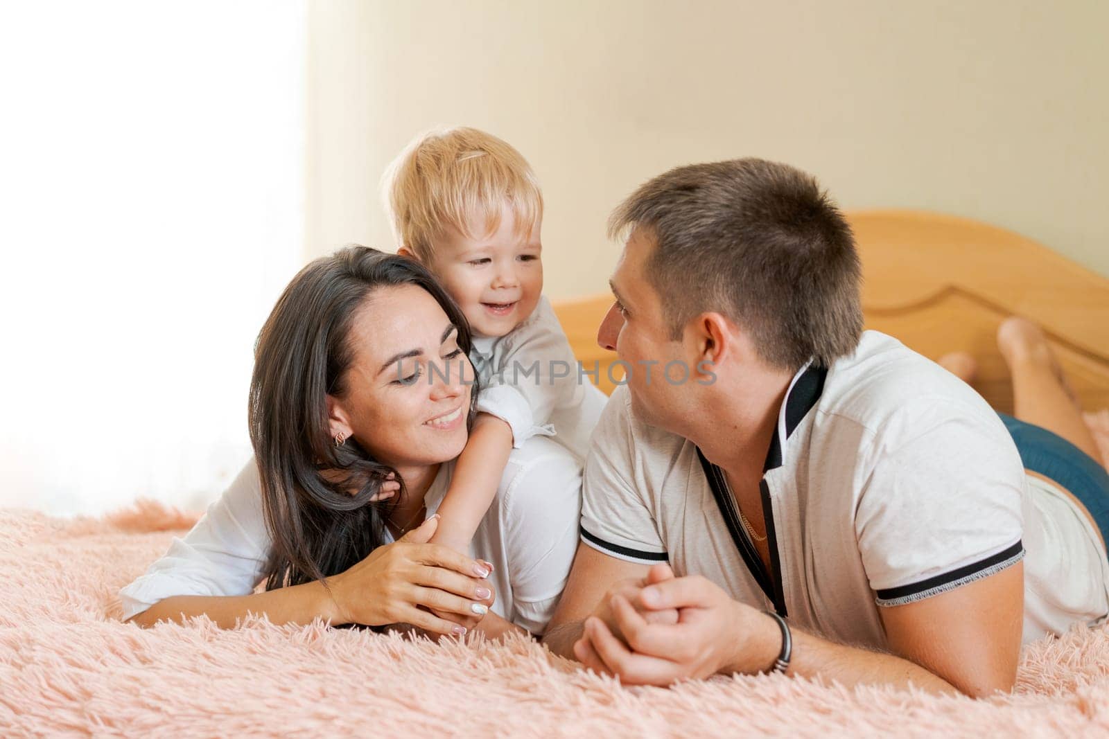 happy family lying on the bed and hugging, mom dad and little son