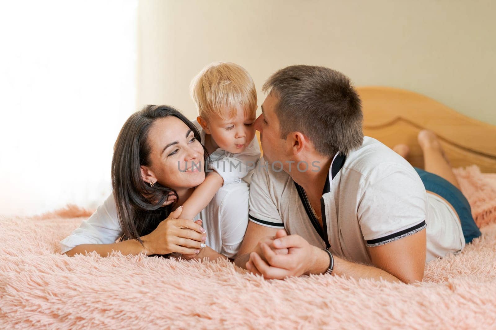 happy family lying on the bed and hugging, mom dad and little son by EkaterinaPereslavtseva