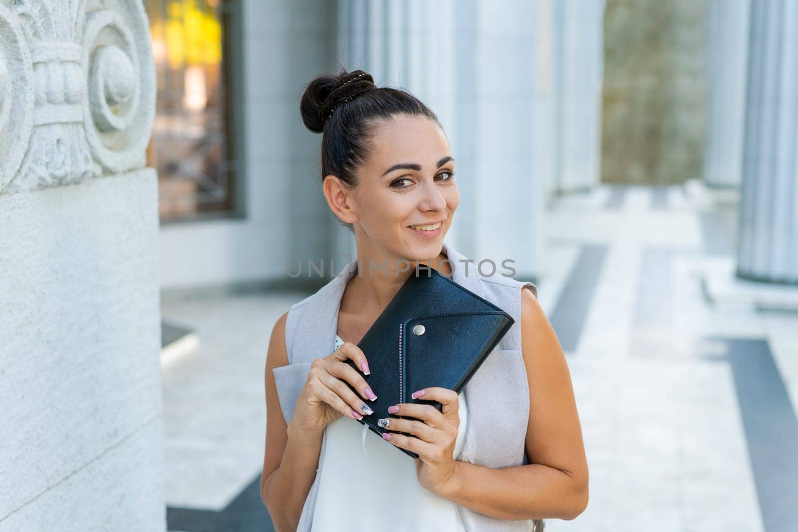 Beautiful woman smiling happy standing at city. Notepad in hand standing on street, in stylish clothes