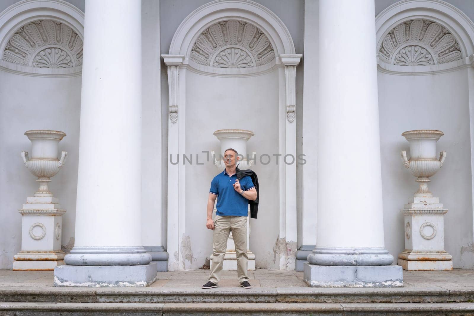 a man in casual clothes stands near the columns of a white building by EkaterinaPereslavtseva