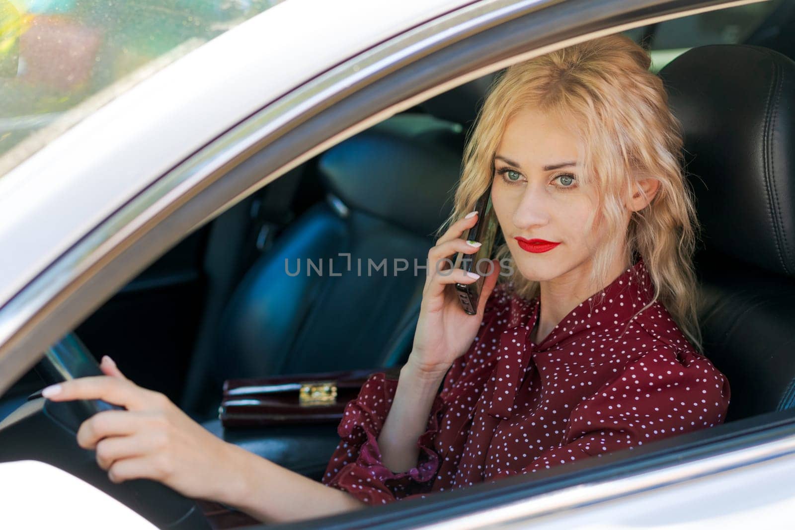 portrait of a beautiful blonde woman in a red dress sitting in a car with a phone by EkaterinaPereslavtseva