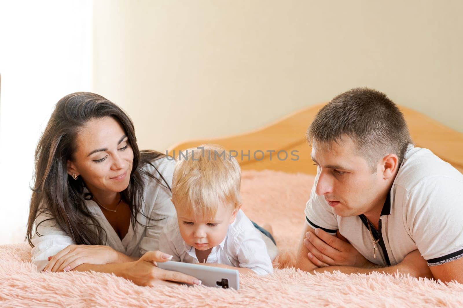 happy family lying on the bed looking at the phone, mom dad and little son