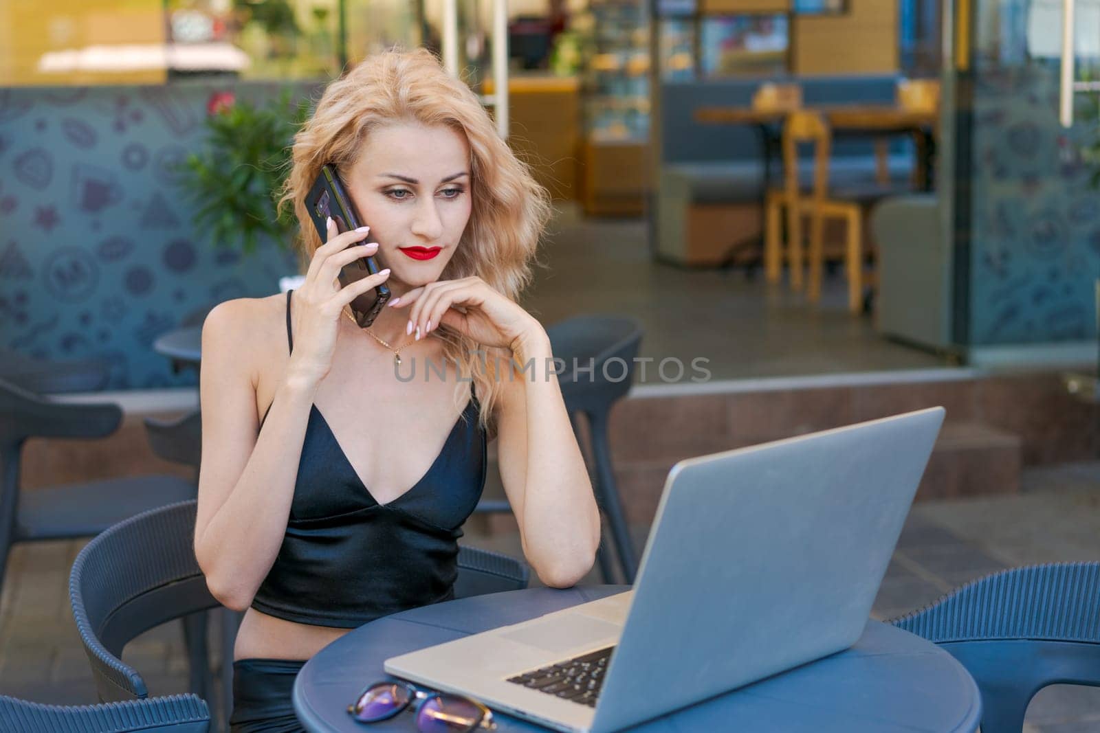 Beautiful woman in glasses sits at table in a street cafe and works on tablet by EkaterinaPereslavtseva