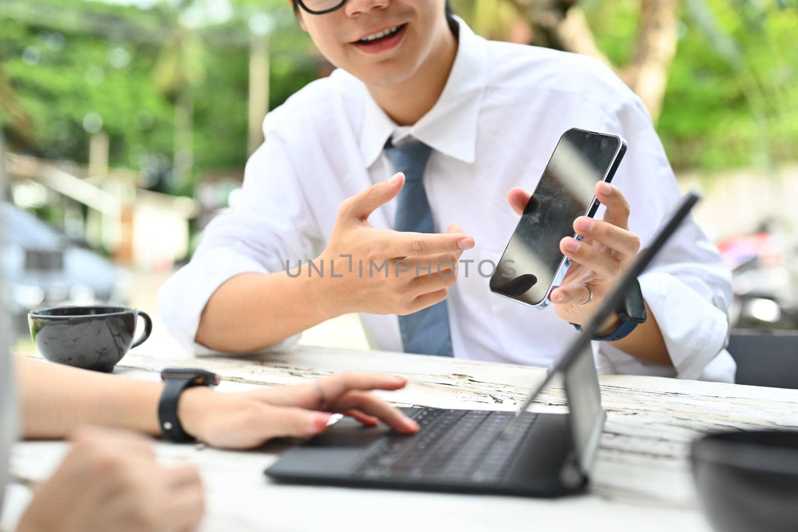 Smiling male office worker share social media news to his colleague during coffee break near office building by prathanchorruangsak