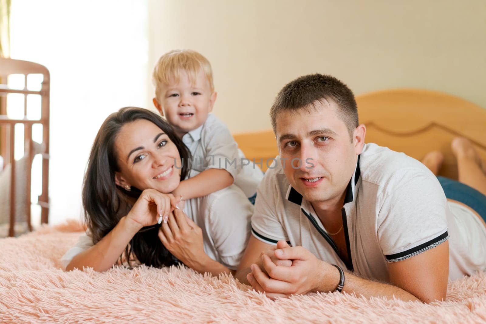 happy family lying on the bed and hugging, mom dad and little son
