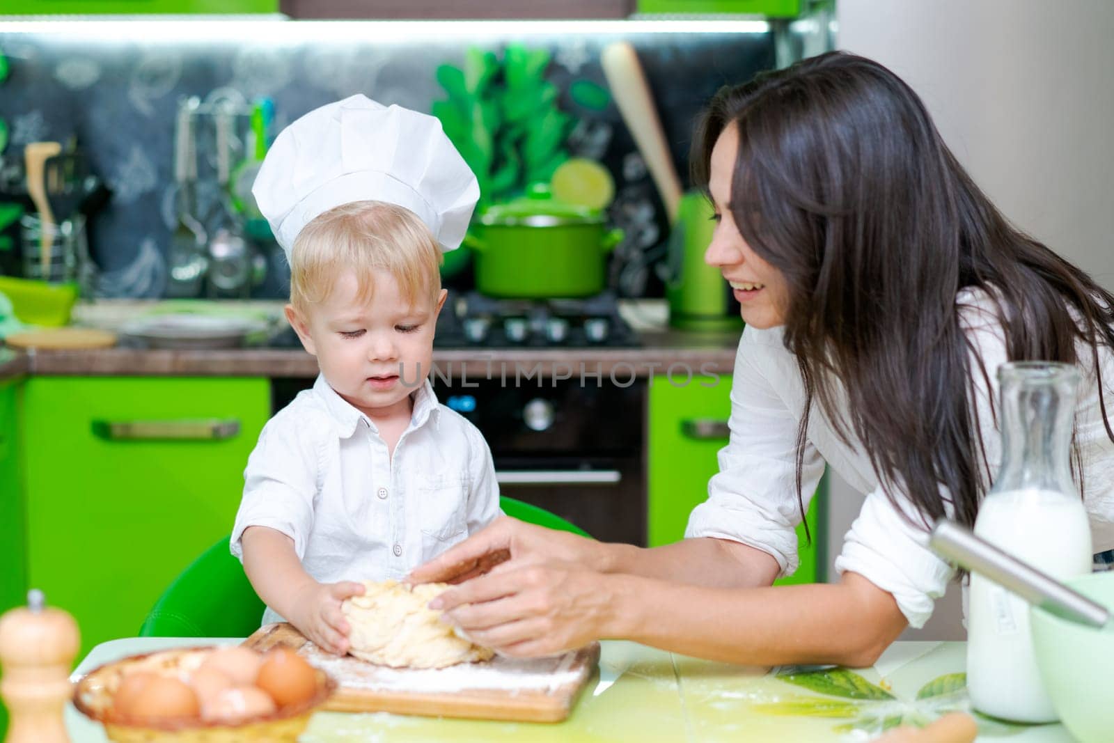 happy family mother and little son preparing dough in kitchen at table. products for dough are on table by EkaterinaPereslavtseva