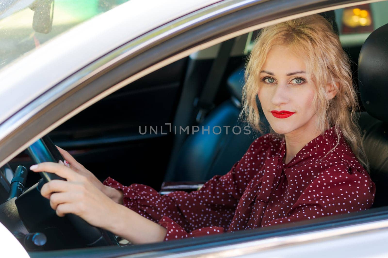 beautiful successful blonde woman in a red dress sitting in a car behind the wheel by EkaterinaPereslavtseva