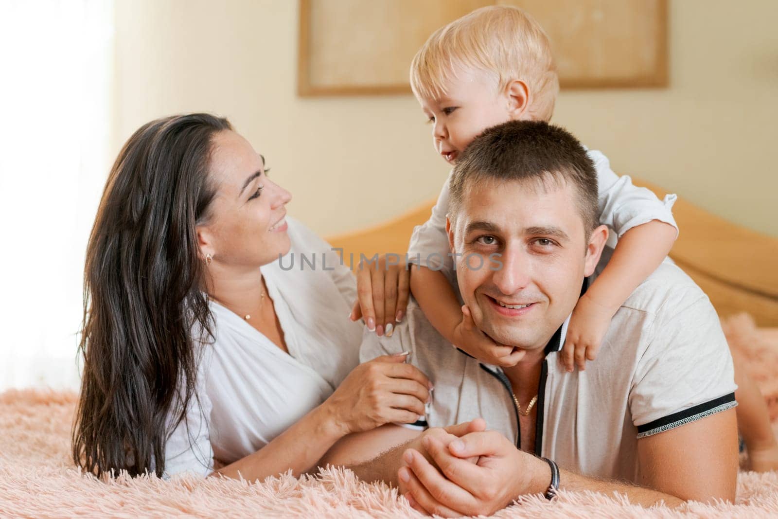 happy family lying on the bed and hugging, mom dad and little son