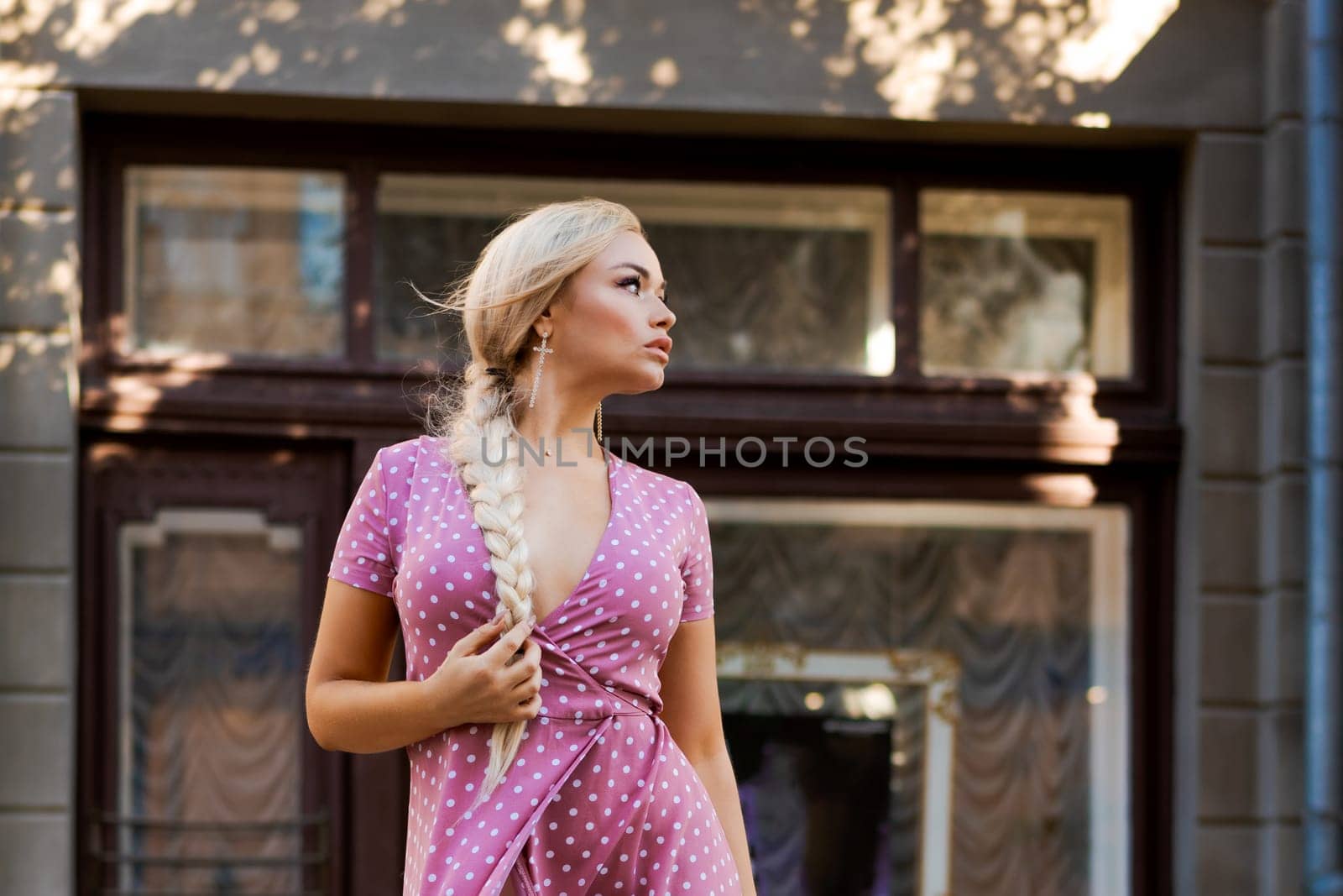 beautiful woman with long braid in pink dress with white polka dots posing on street in the city by EkaterinaPereslavtseva