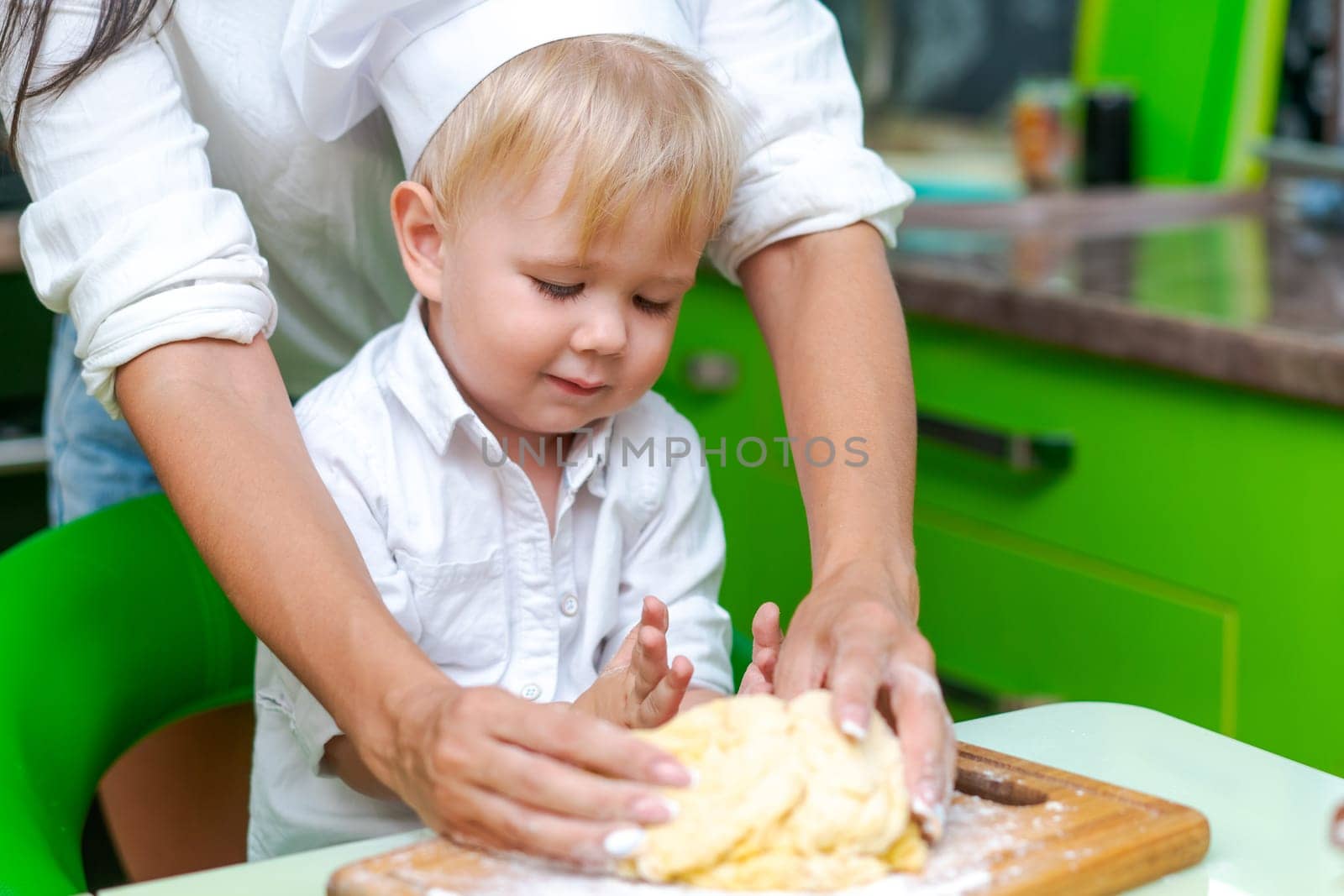happy family mother and little son preparing dough in kitchen at table. products for dough are on table