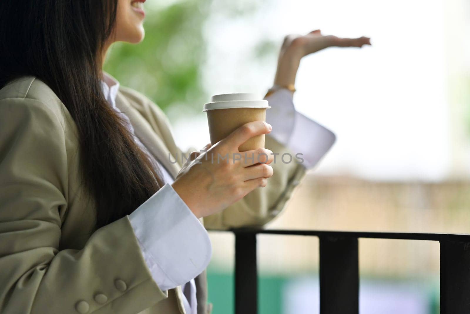 Relaxed businesswoman with paper cup of coffee catching raindrops with hand on office balcony.