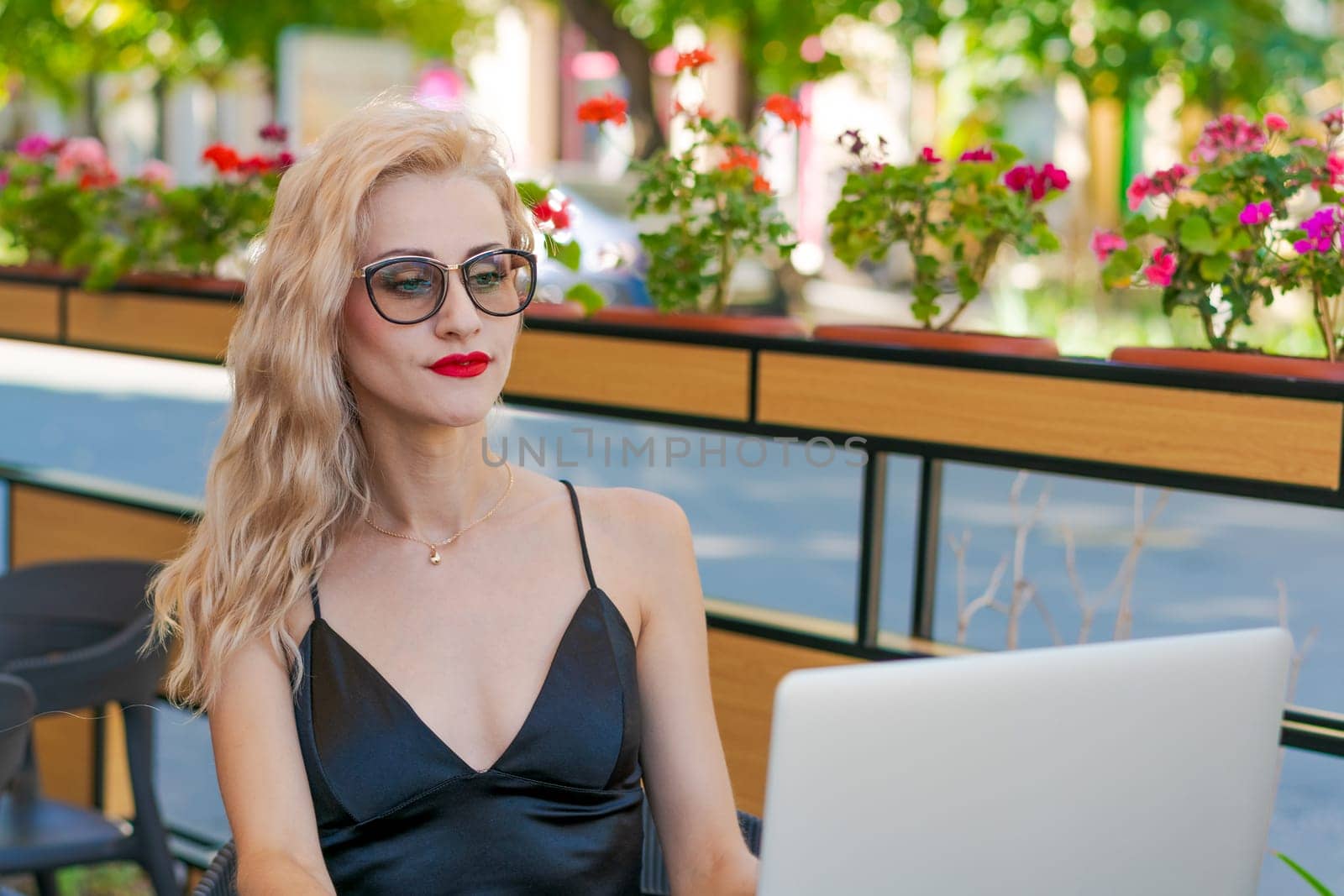 Beautiful woman in glasses sits at table in a street cafe and works on tablet by EkaterinaPereslavtseva