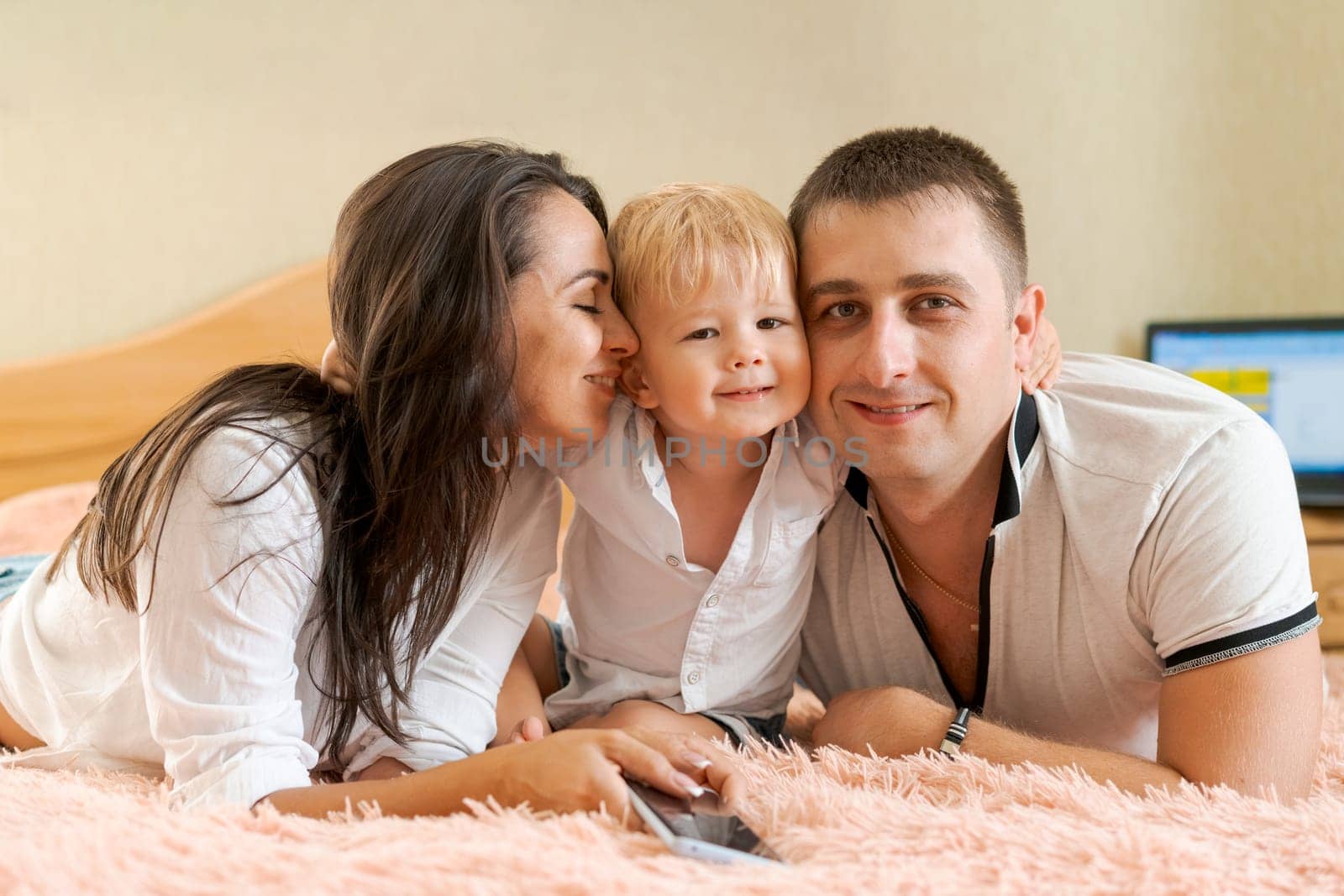 happy family lying on the bed and hugging, mom dad and little son by EkaterinaPereslavtseva